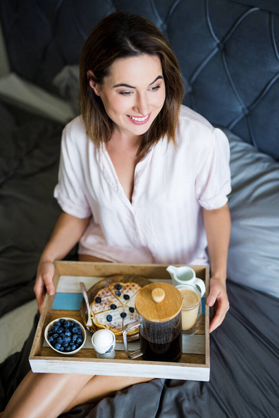 reggeli és reggeli koncepció - boldog nő pizsamában ül az ágyon, és tartja tálca reggelivel - Fotó, kép