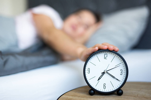утренняя концепция - молодая сонная женщина выключает будильник в спальне
 - Фото, изображение