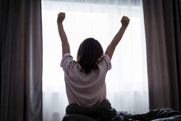 hyvää huomenta konsepti - takaisin näkymä naisen venyttely sängyssä yöpymisen jälkeen ikkunan tausta - Valokuva, kuva