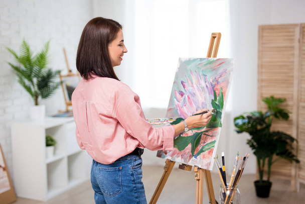 sztuka, kreatywność i koncepcja inspiracji - widok z tyłu malarstwa szczęśliwej kobiety w domu lub studio - Zdjęcie, obraz
