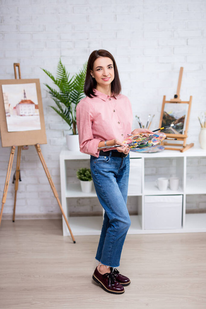 täyspitkä muotokuva nuori nainen taiteilija poseeraa paletti ja sivellin kotona tai studiossa - Valokuva, kuva