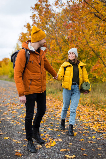 young beautiful couple in love walking in autumn park or forest with backpacks - Photo, Image