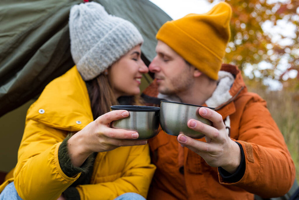 travel, trekking and hiking concept - portrait of cute couple drinking tea or coffee near green tent in autumn forest - Photo, Image