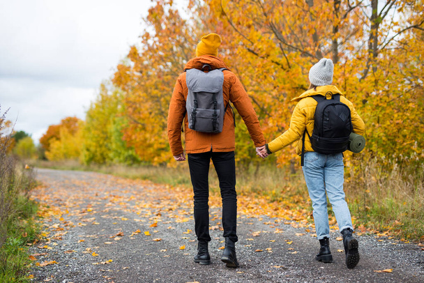 back view of couple hikers with backpacks hiking in autumn forest - Foto, afbeelding