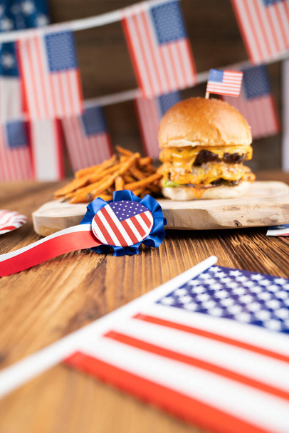 Fourth of July celebration. American flag and decorations. Burgers on rustic wooden table. - 写真・画像