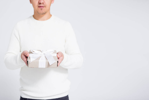 Joulun tai ystävänpäivän konsepti - lahjapaketti, jossa on valkoinen nauha miesten käsissä harmaalla taustalla kopiointitilalla - Valokuva, kuva