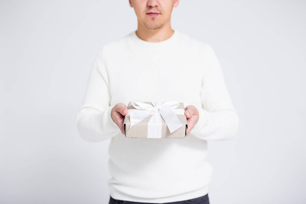 Concepto de Navidad o San Valentín - caja de regalo con cinta blanca en manos masculinas sobre fondo gris con espacio para copiar
 - Foto, imagen