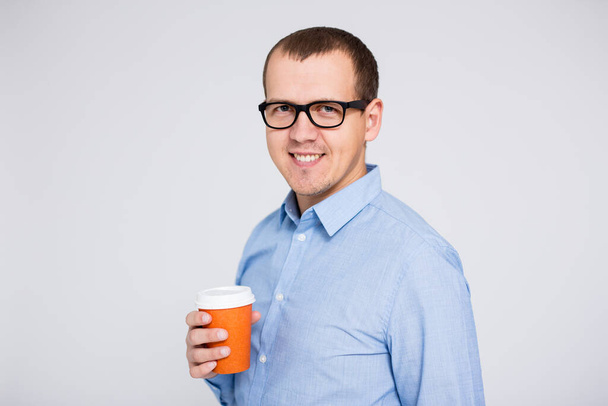 portrait of young businessman in eyeglasses with cup of coffee or tea over gray background - Photo, Image