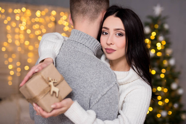 Χριστούγεννα, αγάπη και έκπληξη έννοια - πορτρέτο του ευτυχισμένου νεαρού όμορφου ζευγαριού στην αγάπη σε διακοσμημένο σαλόνι με κουτί δώρου - Φωτογραφία, εικόνα