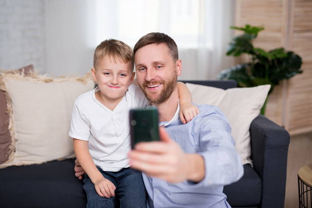 幼い父と息子は自宅のスマートフォンで自撮り写真を撮り - 写真・画像