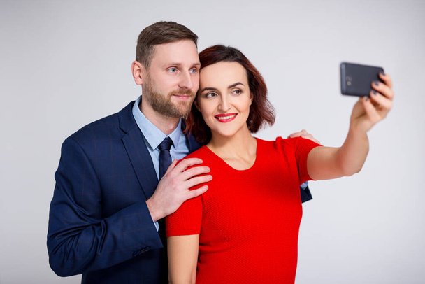 portrait of handsome man and beautiful woman taking selfie photo with smartphone over white background - Photo, image