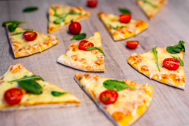 close up of tasty pizza slices with tomatoes and herbs over wooden table background - Fotó, kép