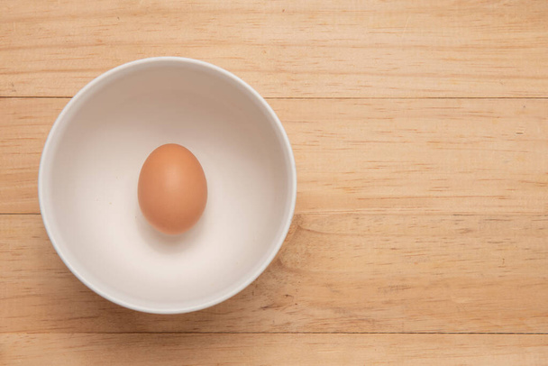 одно куриное яйцо в чашке на светло-коричневом деревянном фоне, Вид сверху с копировальным пространством
 - Фото, изображение
