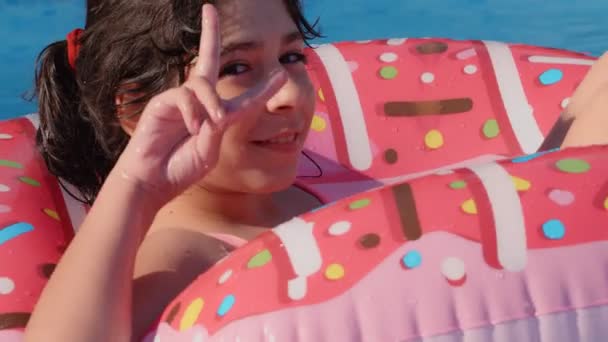 11-12 años de edad feliz linda chica caucásica acostada en un círculo inflable de rosquillas en la piscina en un jardín. Vacaciones frescas de verano para niños y niños. juegos en el agua. Rosado. 4k cámara lenta
 - Metraje, vídeo