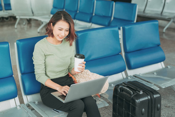 Junge Geschäftsfrau sitzt am Flughafen mit Laptop und trinkt Kaffee. - Foto, Bild