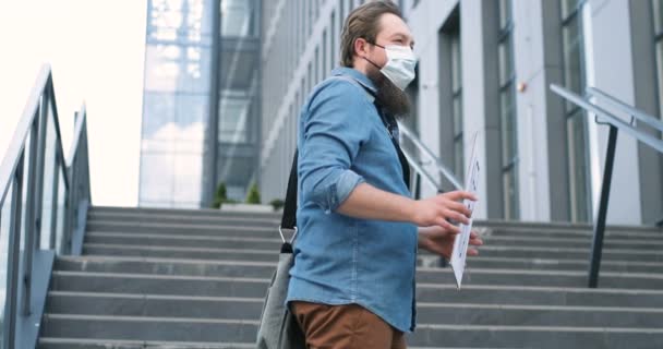 Caucasian young jobless man in medical mask standing outdoor at big stairs and holding carton table with words Need Work. Male demonstrating board with protest against lockdown politics issues. - Séquence, vidéo
