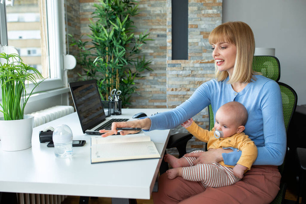 Working from home and holding a baby, mother child concept - Foto, afbeelding
