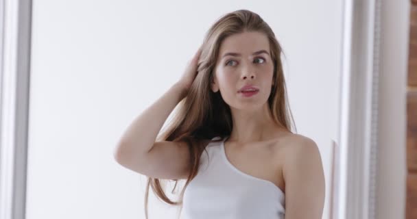 Young woman looking into mirror, preening herself - Felvétel, videó