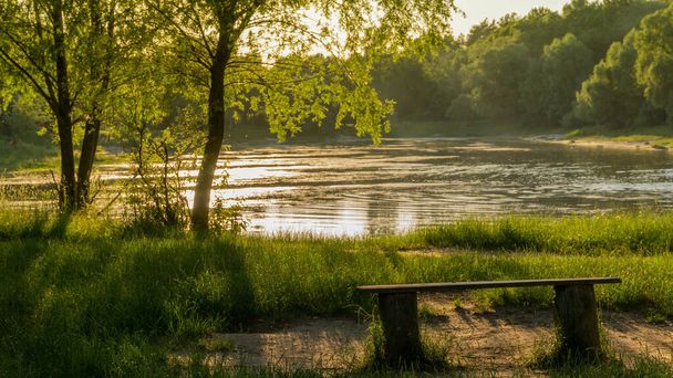 empty bench by the lake in the rays of the setting sun - Photo, Image