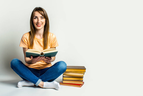 Молодая женщина держит книгу, сидя на полу на светлом фоне. Концепция образования, подготовка к экзаменам. Баннер
. - Фото, изображение