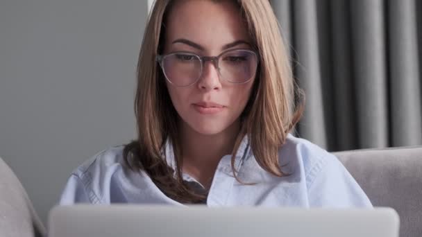 Keskittynyt houkutteleva brunette nainen silmälasit kannettavan tietokoneen kun istuu sohvalla kotona - Materiaali, video