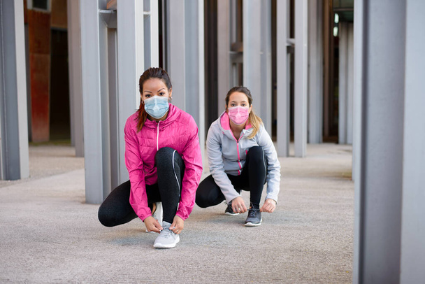 Sporty women wearing face mask and getting ready for urban running ot fitness workout under Covid-19 health crisis keeping social distancing. - Photo, image