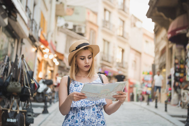 Beautiful young tourist girl in fashionable clothes with map walks around at street and explores city in summer season.Traveler Concept image - Фото, изображение