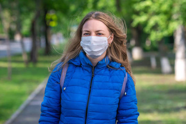 Caucasian blonde woman in protective mask and gloves is walking along empty street. Lifestyle and safe behavior during a coronavirus pandemic. New normal and modern reality 2020. security measures - Foto, imagen