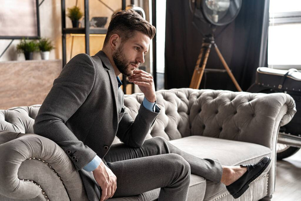 Cool and handsome. Good looking young man in full suit sitting on the sofa while spending time indoors. - Foto, Bild