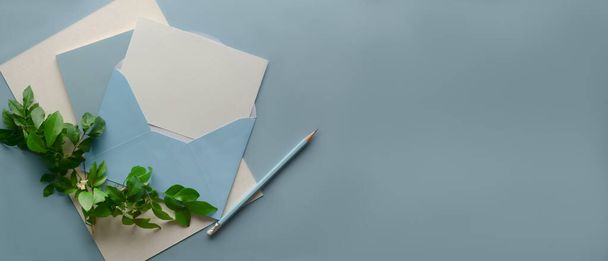 Vista dall'alto del biglietto di auguri, busta blu, matita, spazio per copiare e foglie decorate su sfondo azzurro - Foto, immagini