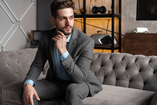 Cool and handsome. Good looking young man in full suit sitting on the sofa while spending time indoors. - Fotografie, Obrázek