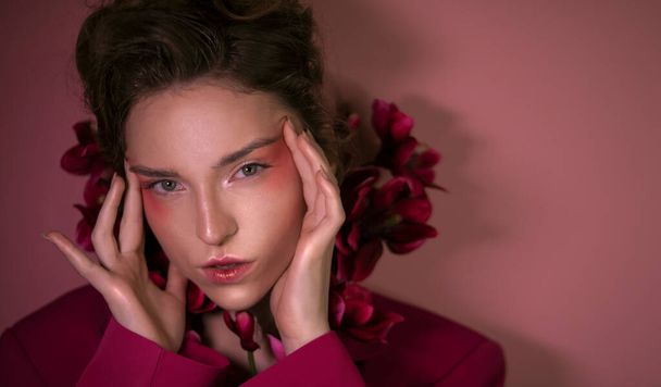 Luxusní dívka s krásnou růžovou make-up v purpurové bundě a s květinami na růžovém pozadí. Dobré pro salóny krásy, transparenty, plakáty, letáky. - Fotografie, Obrázek