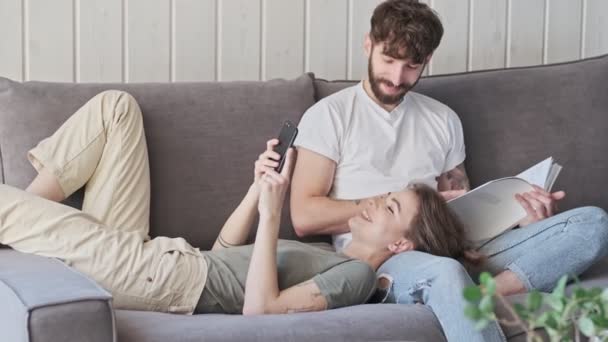 A positive cheerful young couple man and woman are spending time together in the living room at home - Imágenes, Vídeo