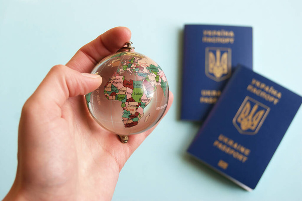 Mano femenina sosteniendo un globo terráqueo en el fondo de dos pasaportes biométricos ucranianos
. - Foto, Imagen