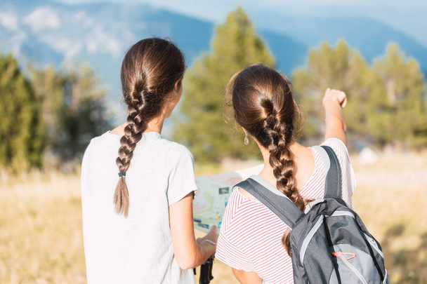 two young travelers with a map pointing to a beautiful place in the mountains - Photo, Image