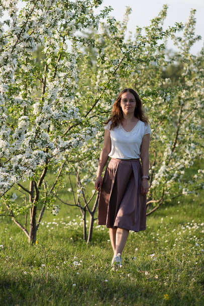 Красива жінка стоїть біля квітучої яблуні у весняному саду. усміхнена красива дівчина на відкритому повітрі
. - Фото, зображення