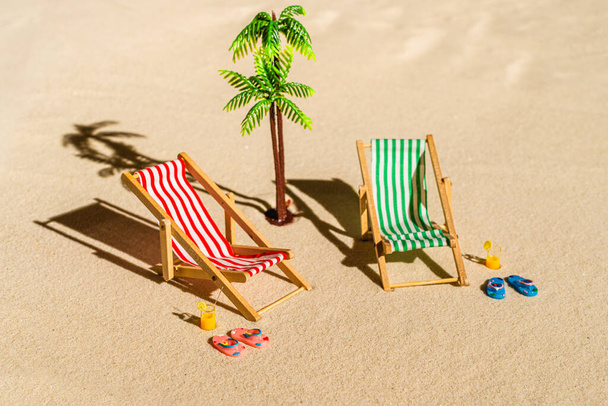 Aerial view of two deck chair, sunbed, lounge, glass of orange juice, flip flops, palm tree on sandy beach. Summer and travel concept. Minimalism - Fotografie, Obrázek