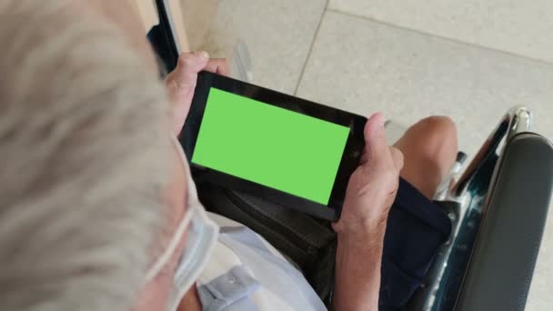 4K záběry v reálném čase zdravotně postižené asijské starý muž na sobě lékařské masky držení digitální tablet s chroma klíč zelené obrazovce pozadí sedí na invalidním vozíku  - Záběry, video
