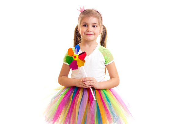 Κοριτσάκι σε πολύχρωμη φούστα και παιχνίδι ανεμόμυλων κοιτάζοντας στην κάμερα - Φωτογραφία, εικόνα