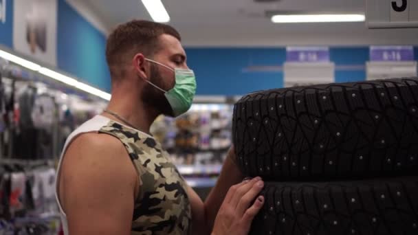 Un hombre con una máscara antiviral médica en una tienda elige neumáticos de coche
. - Imágenes, Vídeo