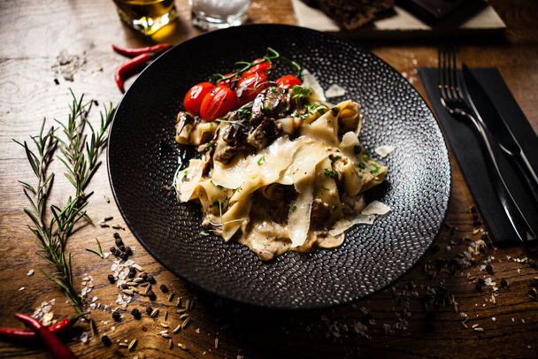 Ζυμαρικά με μαύρο Angus pappardelle με μοσχάρι, champignon και παρμεζάνα σε μαύρο πιάτο. Νόστιμο υγιεινό μεσογειακό παραδοσιακό φαγητό closeup σερβίρεται σε ένα τραπέζι για μεσημεριανό γεύμα στη σύγχρονη κουζίνα - Φωτογραφία, εικόνα