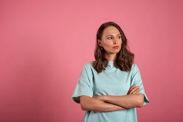 Portrait of a upset girl standing with arms folded over a pink background - Фото, зображення