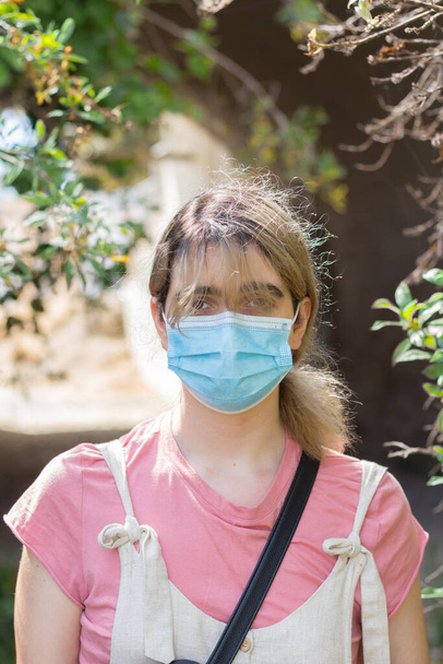 Um retrato de uma mulher com uma máscara facial cercada por plantas em um dia ensolarado
 - Foto, Imagem