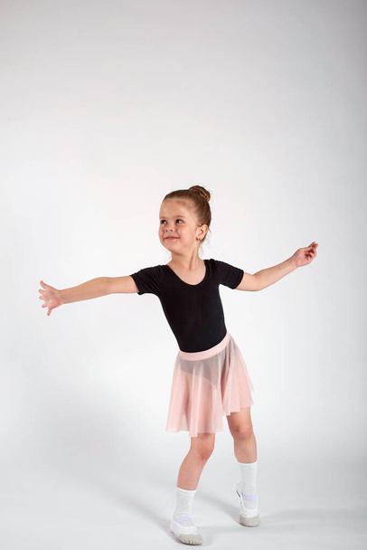 Little girl dressed in dance uniform is dancing over a white background in the studio. - Foto, afbeelding