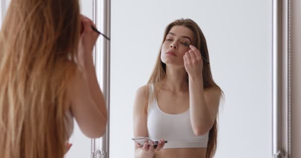 Fiatal nő néz tükörbe, és alkalmazza a szemhéjpúder - Felvétel, videó