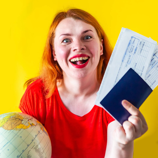 Porträt eines schönen rothaarigen Mädchens mit Globus und Dokumenten auf gelbem Hintergrund, Reisekonzept - Foto, Bild