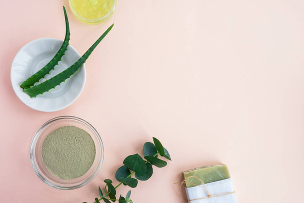 Beauty skincare ingredients. Bowl with clay, aloe, cream gel, handmade soap and eucalyptus leaves on pastel background. Natural organic cosmetics concept. Top view, flat lay, copy space - 写真・画像