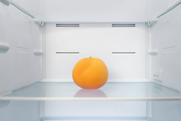 Single bright orange grapefruit into empty fridge - Fotó, kép