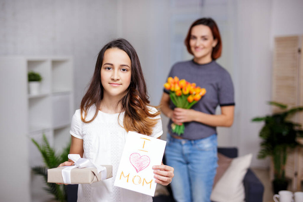 anya nap koncepció - aranyos lánya, hogy meglepetés anya ajándékdobozzal és kézzel készített üdvözlőkártyával - Fotó, kép