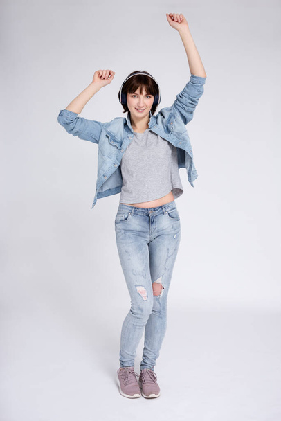 full length portrait of happy teenage girl with braces on teeth listening music in headphones and dancing or celebrating something over gray background - Foto, imagen